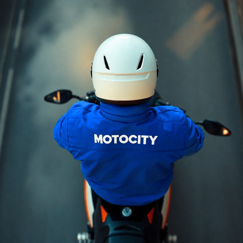Motorista Motocity de espaldas, vista aérea, con la chaqueta corporativa Motocity
